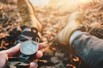 Man traveler hold compass in hand on background legs in hiking boots. Blurred background. Flare...