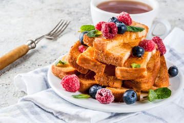 Healthy summer breakfast, baked french toasted bread sticks with fresh berry and honey, morning light grey stone background copy space