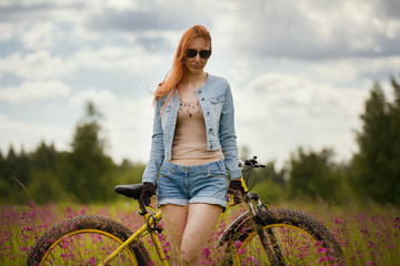Happy young woman with bike in a summer flower field