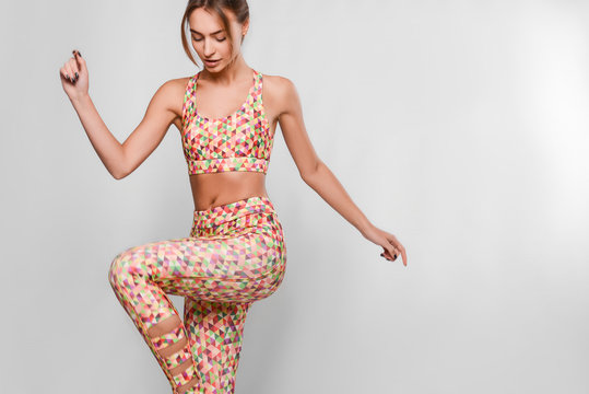 Slim young woman in sport outfit, tight colorful leggings and top with geometrical patterns in a motion, happy, joyful, jumping, isolated in studio