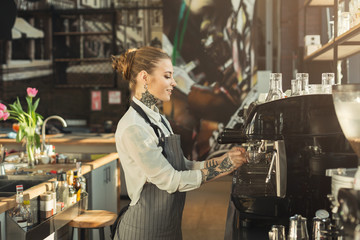 Fototapeta na wymiar Tattooed barista making coffee in professional coffee machine
