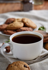 Morning coffee in white cup, chocolate chips cookies on cutting board close-up, selective focus