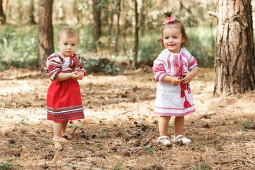 Two baby girls in traditional ukrainian dresses playing in spring forest