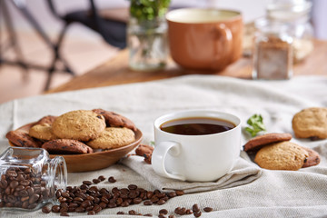 Morning coffee in white cup, chocolate chips cookies on cutting board close-up, selective focus