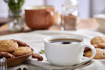 Morning coffee in white cup, chocolate chips cookies on cutting board close-up, selective focus