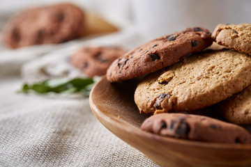 Side view of chocolate chip cookies on a wooden plate over rustic background, selective focus