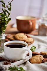 Morning coffee in white cup, chocolate chips cookies on cutting board close-up, selective focus