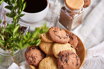 Morning coffee in white cup, chocolate chips cookies on cutting board close-up, selective focus