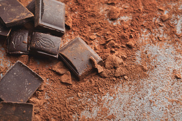 Crushed chocolate bar pieces and cocoa on gray background