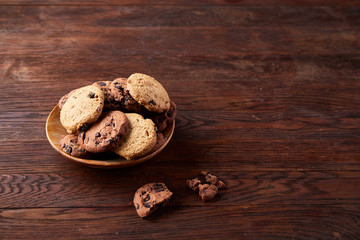 Side view of chocolate chip cookies on a wooden plate over rustic background, selective focus