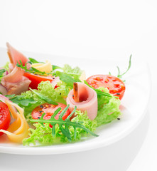 Fresh salad with tomatoes, arugula, cheese and ham on the white plate and white background