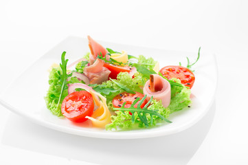 Fresh salad with tomatoes, arugula, cheese and ham on the white plate and white background