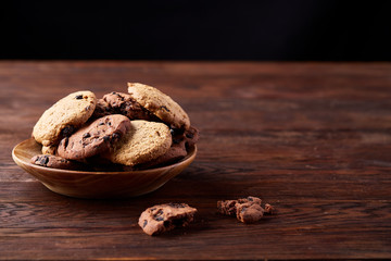 Side view of chocolate chip cookies on a wooden plate over rustic background, selective focus
