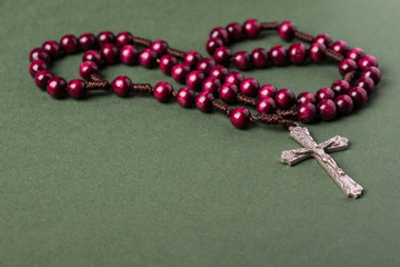 Pink Rosary on a green background with space for writing Christian cross.