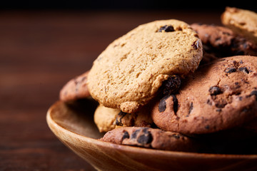 Side view of chocolate chip cookies on a wooden plate over rustic background, selective focus