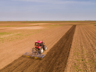 Obraz premium Aerial shot of a tractor cultivating field at spring