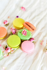 Delicate Fresh Colorful French Macaroons In Pastel Colors With Flowers Roses On A Light Textile Background, Top View