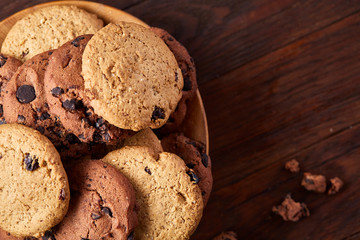 Side view of chocolate chip cookies on a wooden plate over rustic background, selective focus