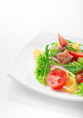 Fresh salad with tomatoes, arugula, cheese and ham on the white plate and white background