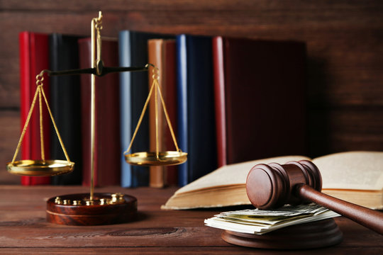 Judge gavel with dollars, books and scales on wooden table