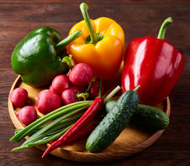 Wooden plate with vegetables for a vegetarian salad on rustic wooden background, close-up, selective focus