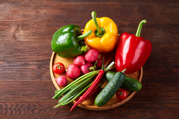 Wooden plate with vegetables for a vegetarian salad on rustic wooden background, close-up, selective focus