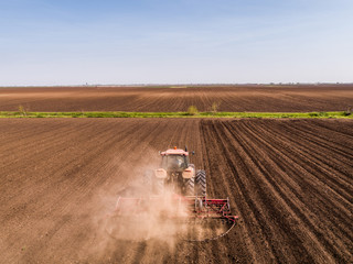 Obraz premium Aerial shot of a tractor cultivating field at spring
