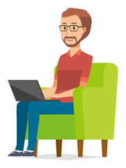 A bearded man wearing eyeglasses is sitting on a sofa and operating a laptop computer