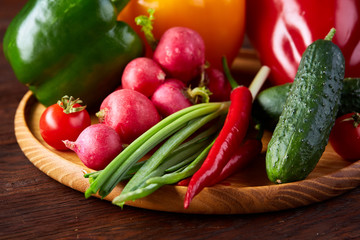Wooden plate with vegetables for a vegetarian salad on rustic wooden background, close-up, selective focus
