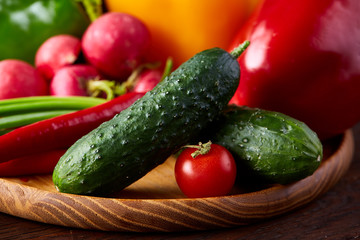 Wooden plate with vegetables for a vegetarian salad on rustic wooden background, close-up, selective focus