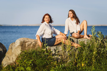 two women sit on the rocks on the coast in the summer