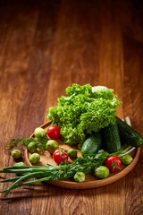 Vegetarian still life of fresh vegetables on wooden plate over rustic background, close-up, flat lay.