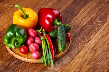 Wooden plate with vegetables for a vegetarian salad on rustic wooden background, close-up, selective focus