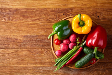 Wooden plate with vegetables for a vegetarian salad on rustic wooden background, close-up, selective focus