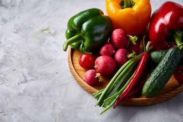 Wooden plate with vegetables for a vegetarian salad on white textured background, close-up, selective focus