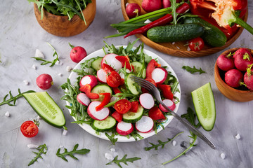 Wooden plate with vegetables for a vegetarian salad on white textured background, close-up, selective focus
