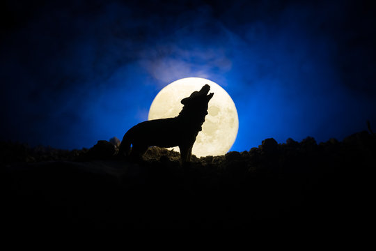Silhouette of howling wolf against dark toned foggy background and full moon or Wolf in silhouette howling to the full moon. Halloween horror concept.