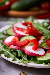 Wooden plate with vegetables for a vegetarian salad on white textured background, close-up, selective focus