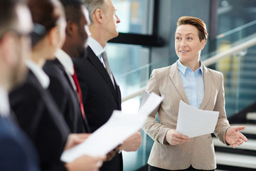 Confident female business leader with papers making report about the latest upgrades of financial...