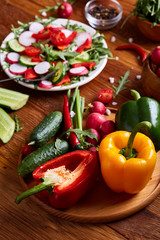 Fresh red radish in wooden bowl among plates with vegetables, herbs and spicies, top view, selective focus.