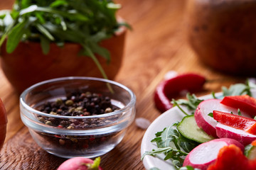 Fresh red radish in wooden bowl among plates with vegetables, herbs and spicies, top view, selective focus.
