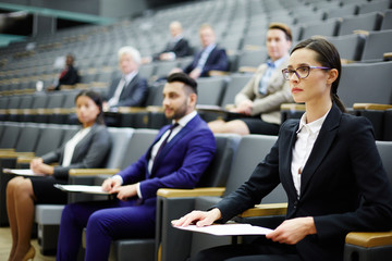 Young businesswoman and her colleagues sitting in armchairs of conference hall and listening to...