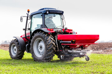 Farmer in tractor fertilizing wheat field at spring with npk
