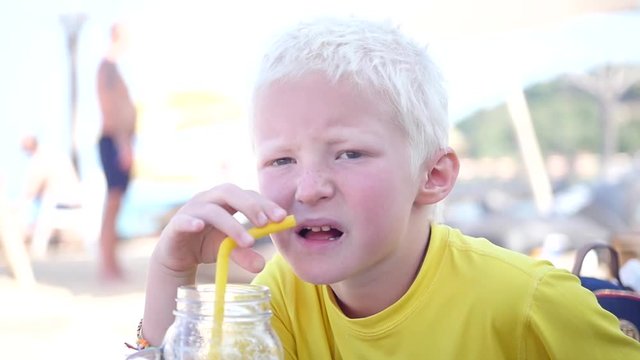 A young blond boy drinks a cocktail on the beach from a yellow tube. slow motion. 1920x1080. full hd