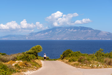 Unidentified tourists walking along a road with a view of the sea and Kefalonia island in distance. Zakynthos, Greece