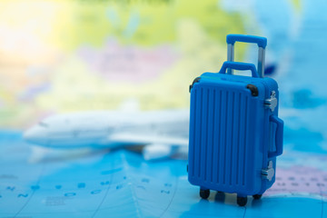 Travel Concept. Blue miniature baggage toy on world map with airplane model as background.