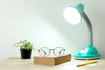 book and glasses is placed on the table with a light lamp at the room. Educational concepts and...