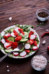 Fresh red radish in wooden bowl among plates with vegetables, herbs and spicies, top view, selective focus.