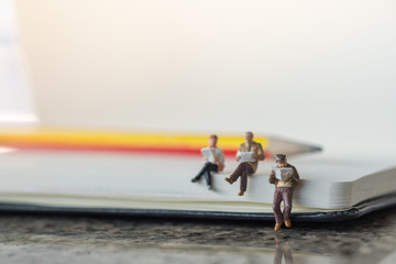 Business, Education concept. Businessman, male and female miniature figures sitting and reading a book on notebook with pencil.