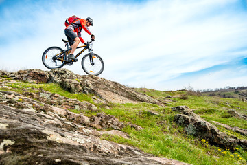 Cyclist in Red Jacket Riding Mountain Bike Down Rocky Hill. Extreme Sport and Adventure Concept.